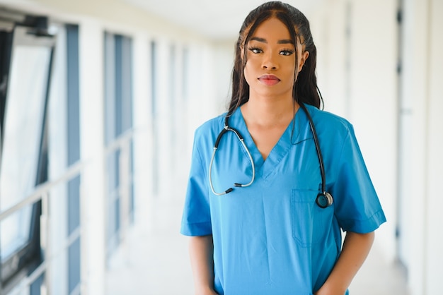 의학, 직업 및 건강 관리 개념 - 병원 배경 위에 청진기를 들고 행복한 미소 짓는 아프리카계 미국인 여성 의사