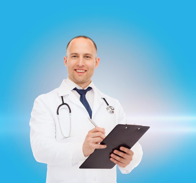 medicine, profession and healthcare concept - smiling male doctor with clipboard and stethoscope writing prescription over blue background