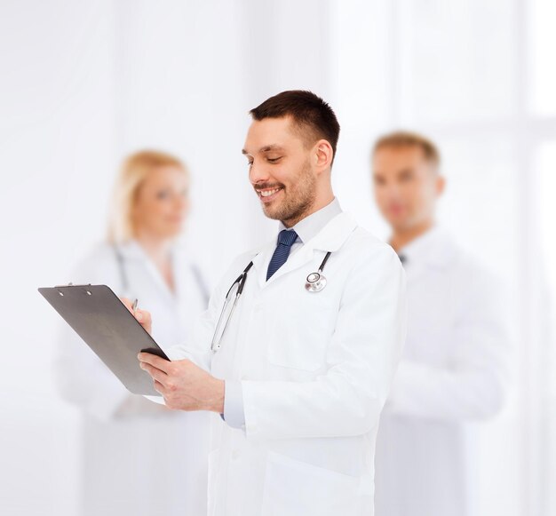 medicine, profession, and healthcare concept - smiling male doctor with clipboard and stethoscope writing prescription over white background