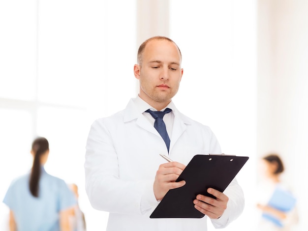 medicine, profession, teamwork and healthcare concept - serious male doctor with clipboard writing prescription over group of medics