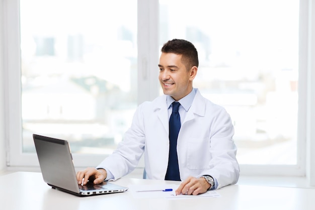 医学、職業、技術、人々 のコンセプト - 医療事務にラップトップで男性医師を笑顔