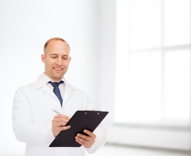medicine, profession, workplace and healthcare concept - smiling male doctor with clipboard writing prescription over white room background