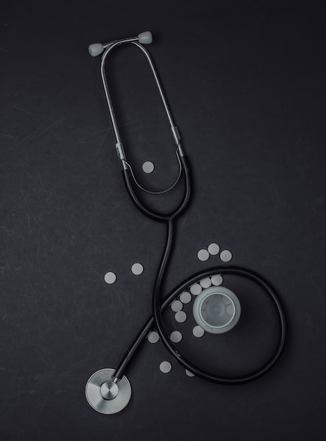 Medicine still life. Stethoscope with bottle of pills on black background. Top view.