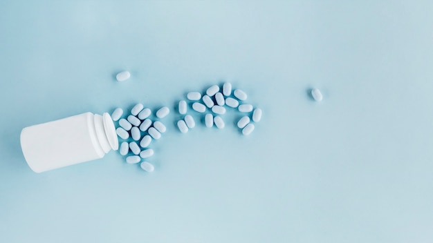 Medicine tablets spilled from bottle over blue background