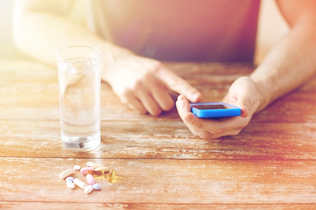 Foto medicina, tecnologia, integratori alimentari e concetto di persone - primo piano di smartphone mani maschili, pillole e acqua sul tavolo