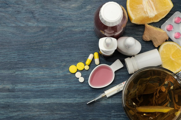 Pillole medicinali sciroppo per la tosse termometro e rimedi popolari per il trattamento dell'influenza e del comune raffreddore su un tavolo di legno blu vista dall'alto