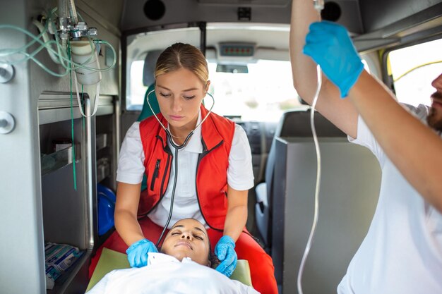 Photo medics with injured patient giving an infusion young male paramedics holding iv solution female doctor listeting heart of patient