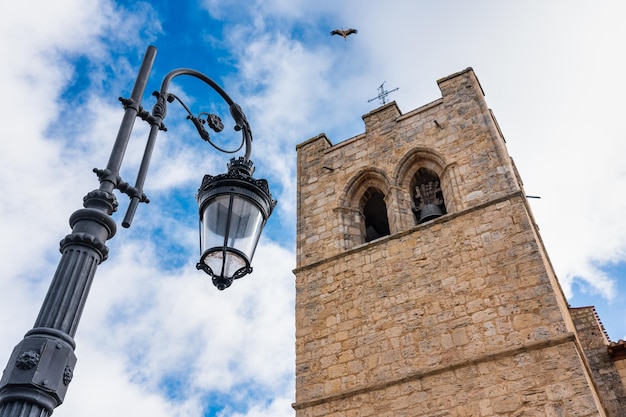 Фото Средневековая церковная башня и электрический уличный фонарь, когда аист летит по небу аранда