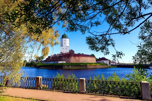 잎이 있는 푸른 하늘을 배경으로 물 위에 있는 비보르크 성(Vyborg Castle)의 중세 요새