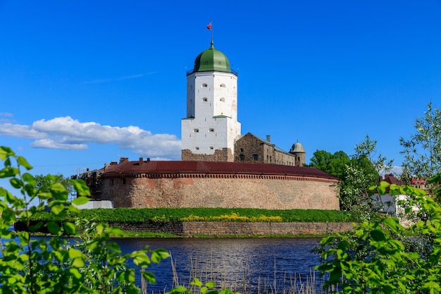 푸른 잎사귀가 있는 푸른 하늘을 배경으로 물 위에 있는 비보르크 성(Vyborg Castle)의 중세 요새