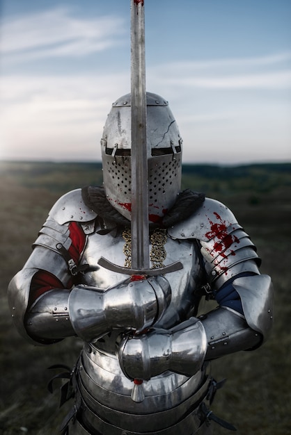 Medieval knight in armor and helmet poses with sword, great battle. Armored ancient warrior in armour posing in the field