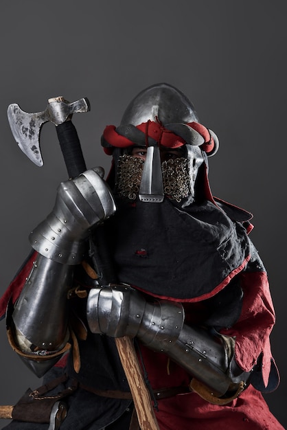 Medieval knight on grey. Portrait of brutal dirty face warrior with chain mail armour red and black clothes and battle axe