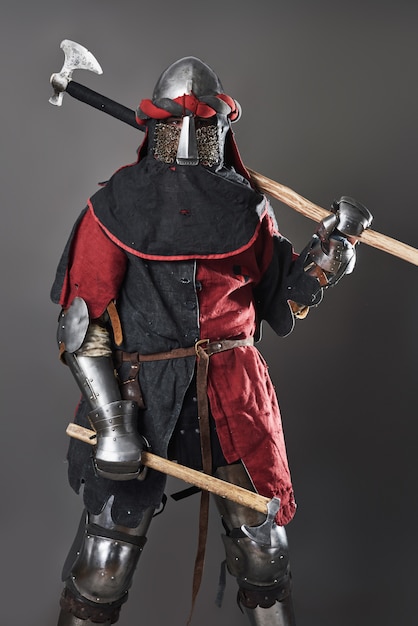 Medieval knight on grey. Portrait of brutal dirty face warrior with chain mail armour red and black clothes and battle axe