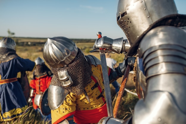 Medieval knights in armor and helmets fight with sword and axe. Armored ancient warrior in armour posing in the field