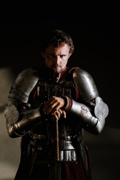Средневековый рыцарь в доспехах и с оружием на темном фоне. Портрет рыцаря