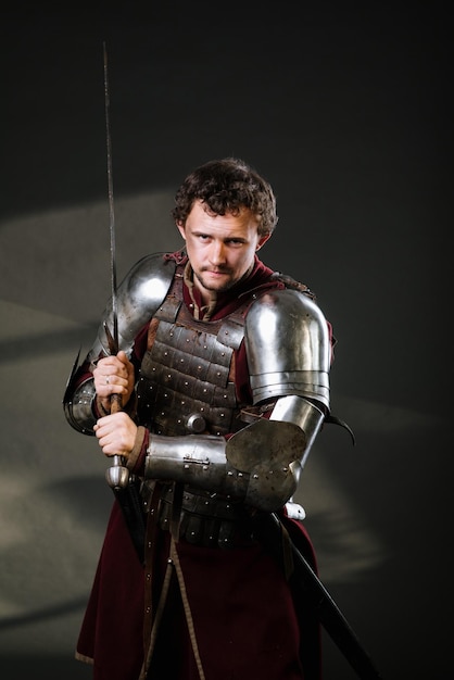 Medieval man knight in armor and weapon on dark background. Portrait of the knight