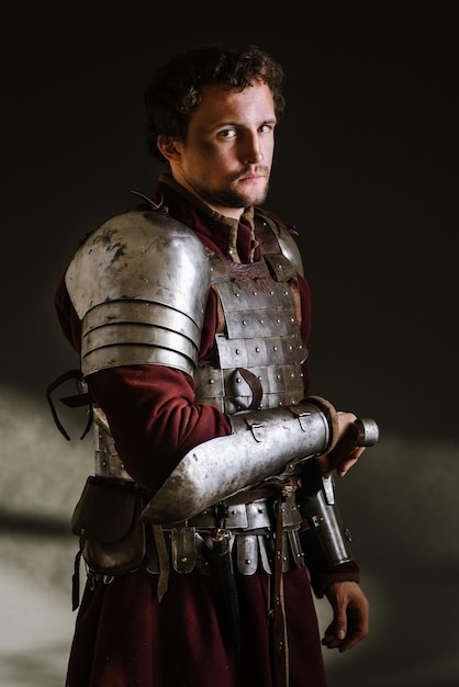 Medieval man knight in armor and weapon on dark background. Portrait of the knight