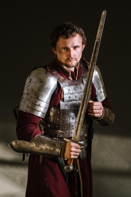 Medieval man knight in armor and weapon on dark background. Portrait of the knight