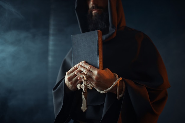 Medieval monk holds book and wooden cross in hands