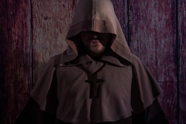 Medieval monk praying with closed eyes with wooden cross in arms