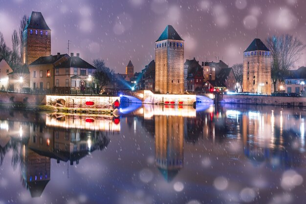 雪の降る夜、ストラスブール、アルザス、フランスのプティットフランスの鏡の反射と中世の塔と橋