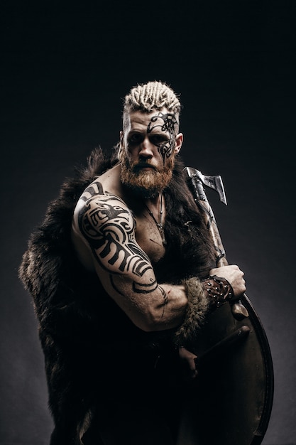 Medieval warrior viking with tattoo beard and braids in hair\
with axe and shield