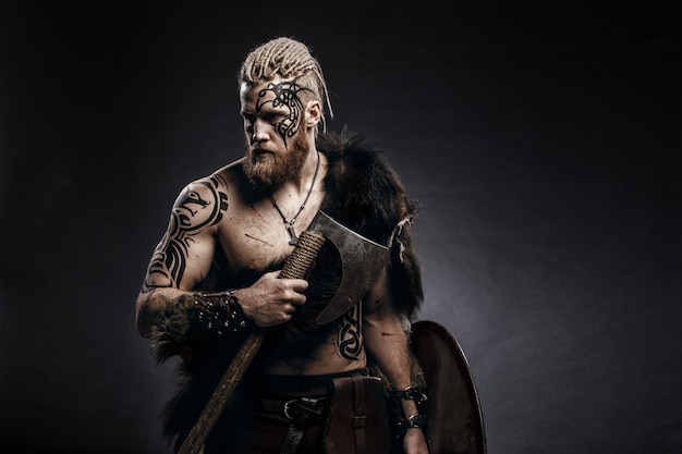 Photo medieval warrior viking with tattoo beard and braids in hair with axe and shield