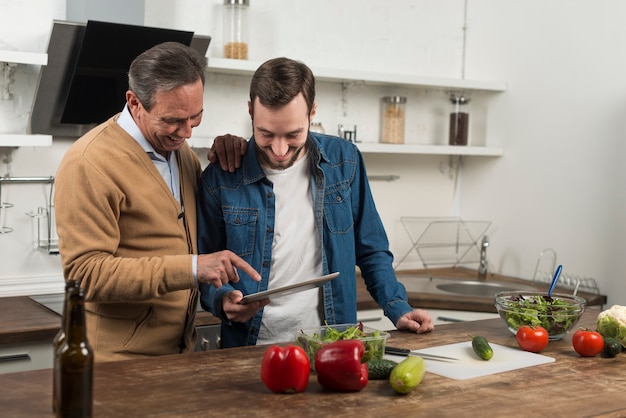 Medio schot vader en zoon die tablet in keuken bekijken