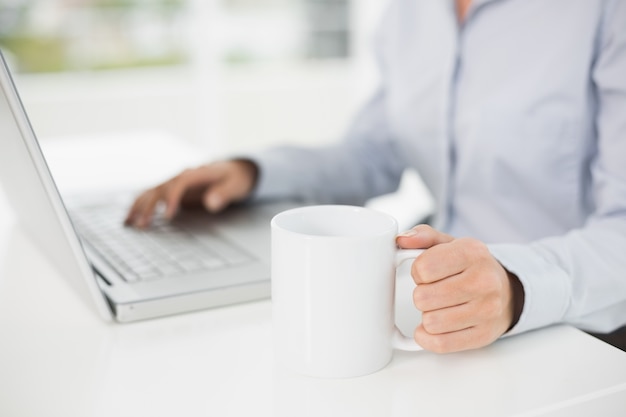 Medio sectie van een onderneemster die laptop met behulp van terwijl het hebben van koffie