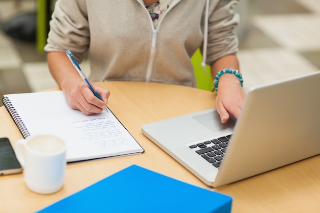 Medio sectie van een vrouwelijke student die thuiswerk door laptop doet