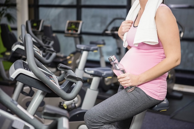 Medio sectie van zwangere vrouw op hometrainer bij de gymnastiek