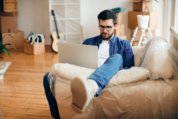 Medio volwassen man die laptop gebruikt terwijl hij ontspant in zijn nieuwe appartement