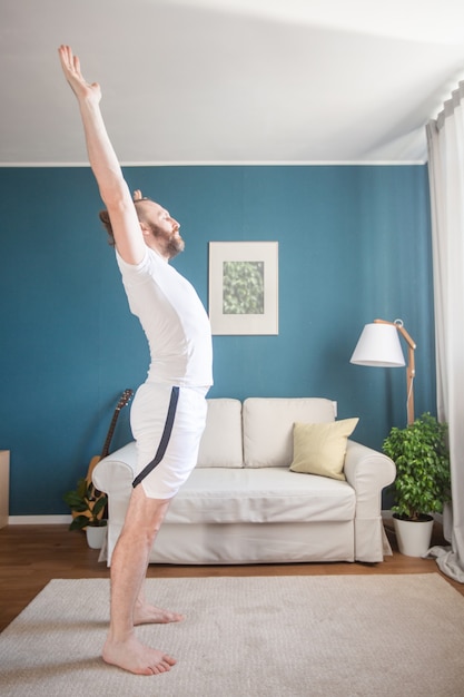Medio volwassen volwassen man in witte sportkleding oefent yoga stretch doen oefeningen thuis minimalistische Scandinavische designkamer