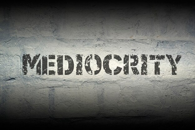 Mediocrity world stencil print on the grunge white brick wall; specially designed font is used