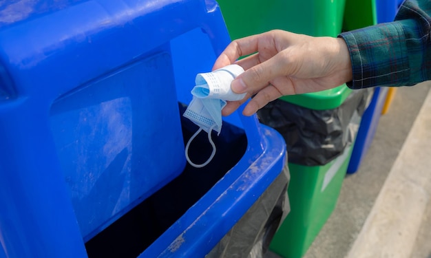 Medisch afval Mensen gooien met de hand gebruikt medisch beschermend gezichtsmasker in de prullenbak Blauw plastic