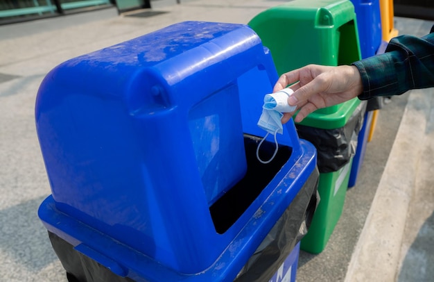 Medisch afval Mensen gooien met de hand gebruikt medisch beschermend gezichtsmasker in de prullenbak Blauw plastic