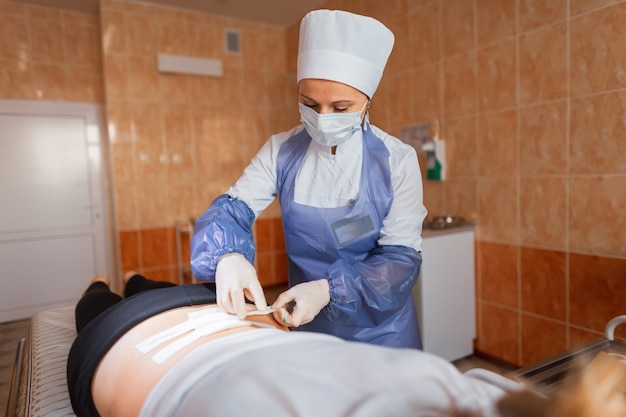 Medisch assistent in een beschermend masker en in medisch uniform verband op de rug toe te passen op de patiënt in de kliniek. Ziekenhuiszorg