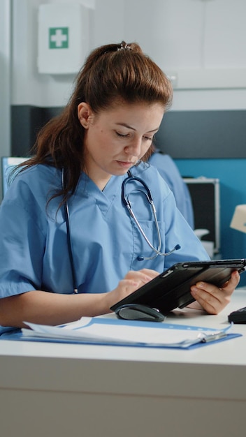 Medisch assistent typt op het tabletscherm en controleert de computer op een afspraak in het spreekkamer. Verpleegkundige die naar de monitor kijkt terwijl ze een moderne gadget gebruikt voor een bezoek aan de gezondheidszorg.