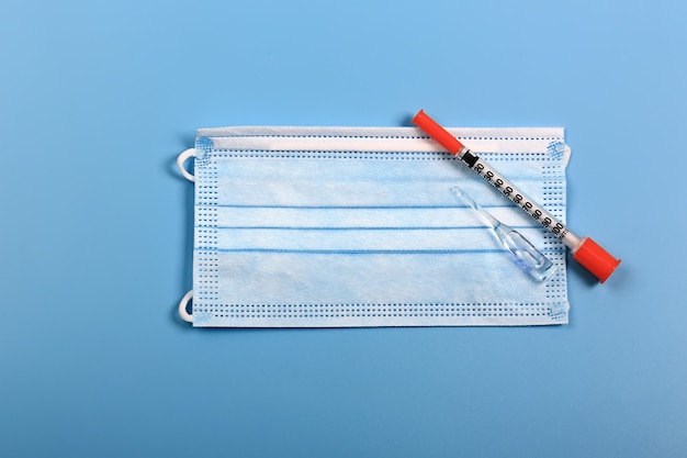 Medisch concept vaccin injectiespuit en medisch masker op een blauwe achtergrond kopie ruimte