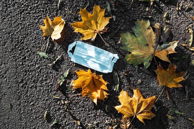 Medisch gezichtsmasker liggend op asfalt met herfstbladeren buitenshuis