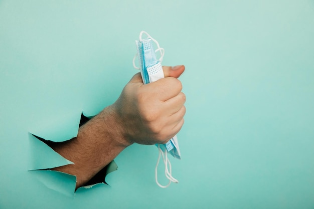 Foto medisch masker in een mannenhand op een blauwe achtergrond met een gat medisch concept