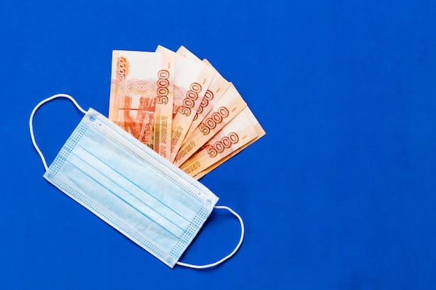 Medisch masker ligt op het geld. Het concept van het verhogen van de prijs van medische maskers. medisch masker en Russisch geld op een blauwe achtergrond. coronamasker