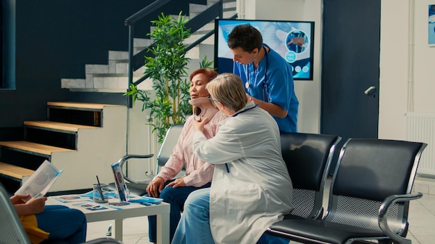 Medisch personeel dat cervicale nekkraag verwijdert van oudere patiënt met breuk, omgaan met fysieke pijn na verwonding. Verpleegkundige en dokter die steun geven aan gewonde vrouw, revalidatietherapie.