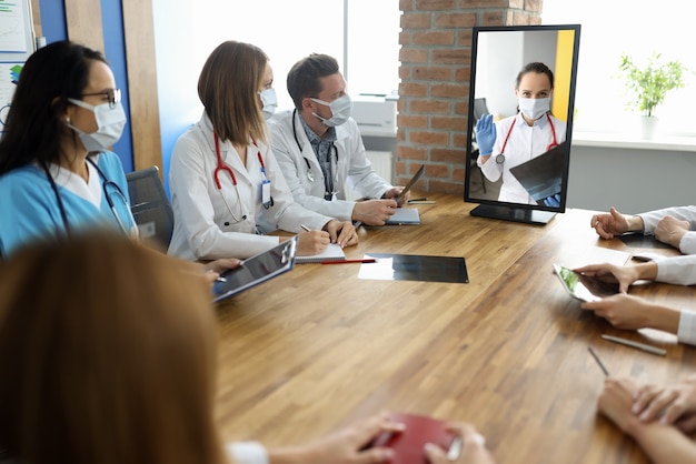 Medisch personeel zit aan tafel met documenten en kijkt naar monitor waarop dokter gesprek ziet