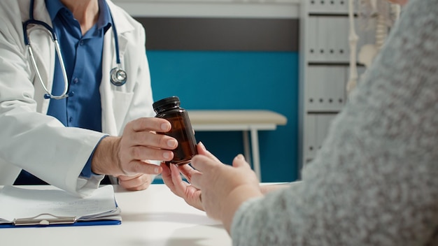 Medisch specialist die ziektebehandeling geeft op voorschrift van de gezondheidszorg, fles met pillen en vitamines toont aan gepensioneerde patiënt voor herstel. Fles met medicijnen en pijnstillers.