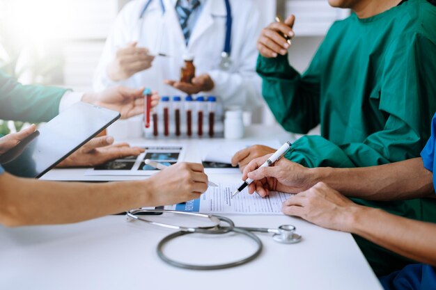 Foto medisch team dat een vergadering heeft met artsen in witte labjassen en chirurgische scrubs die aan een tafel zitten en een patiënt bespreken die online werkt met behulp van computers in de medische industrie