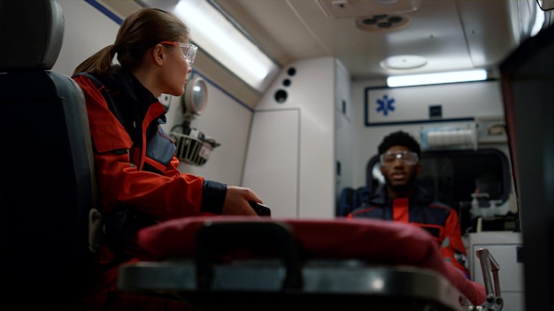Foto medisch team praat over het werk in een spoedeisende hulpvoertuig multiraciale ambulanceartsen rijden op oproep afro-amerikaanse assistent praat met collega vrouwelijke paramedicus leest bericht op smartphone