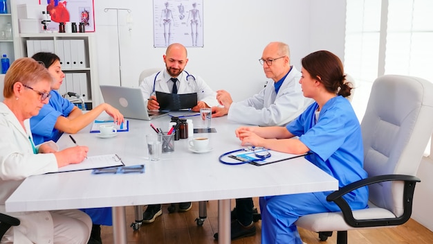 Medisch team zitten en discussiëren over de diagnose van de patiënt in de vergaderruimte van het ziekenhuis. Kliniekdeskundige therapeut in gesprek met collega's over ziekte voor behandelingsontwikkeling, medisch professional