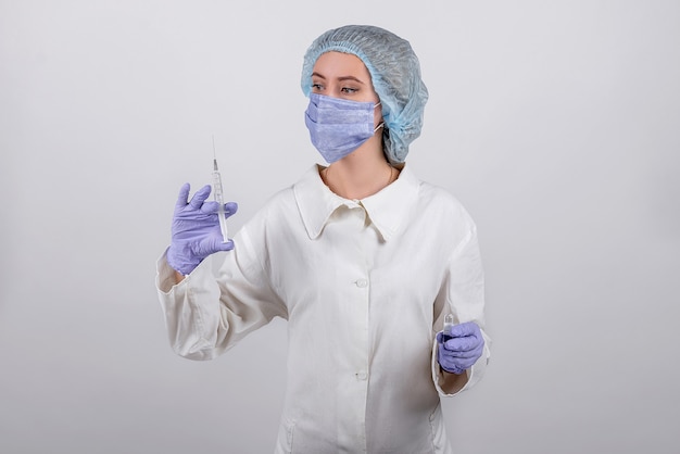 Medisch werker in een masker, blauwe handschoenen en een net houdt een spuit en een ampul in zijn handen