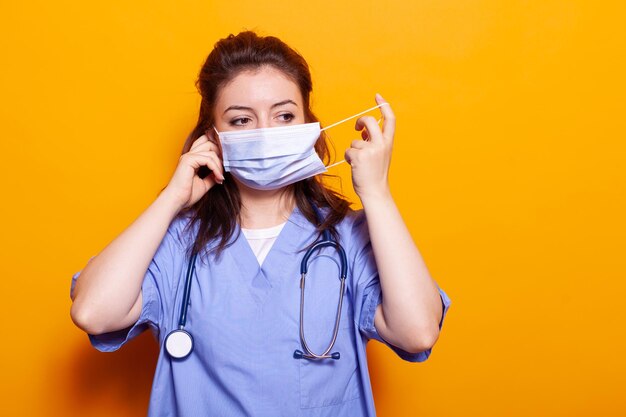 Medische assistent die een beschermend masker op het gezicht zet voor de camera. Vrouwelijke verpleegster die uniform en stethoscoop draagt, met veiligheid en bescherming tegen coronavirus tijdens pandemie.